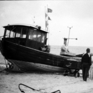 Old fishing boat on shore with two people.
