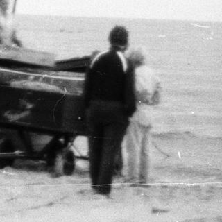Old fishing boat on shore with two people.
