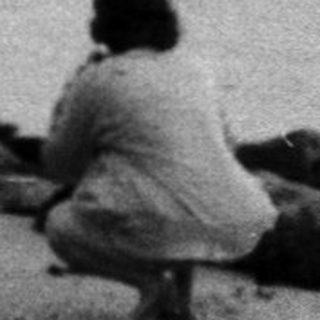 Person sitting alone by ocean waves near breakwater.