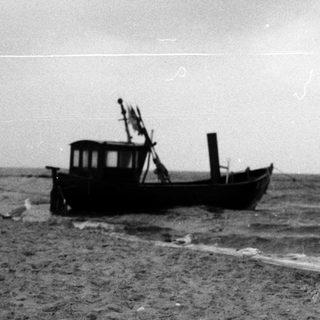 Old boat stranded on sandy beach near waves.