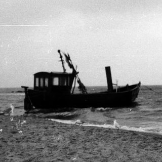 Small boat stranded on sandy beach near waves.