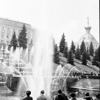 People observing large fountain in grand park setting.