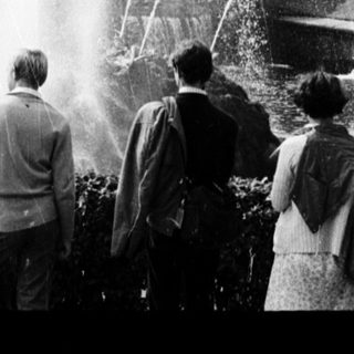 People observing large fountain in grand park setting.
