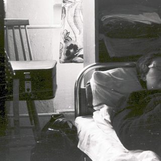 Person reading newspaper in hospital bed.