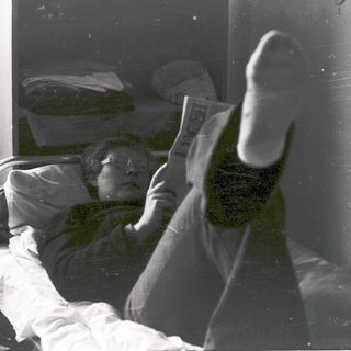 Person reading newspaper in hospital bed.