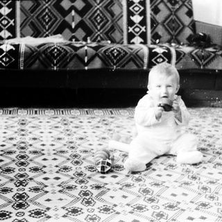 Baby sitting on patterned rug holding toy.