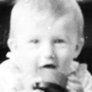 Baby sitting on patterned rug holding toy.