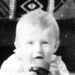 Baby sitting on patterned rug holding toy.