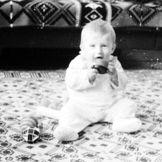Baby sitting on patterned rug holding toy.