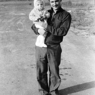 Man holding baby outdoors in vintage clothing.