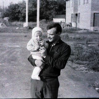 A man holding a baby outdoors in a rural setting.