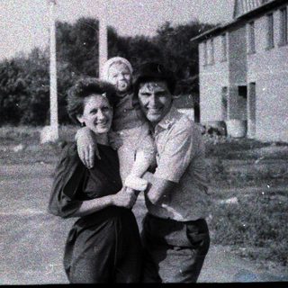 Three people posing happily outdoors in rural setting.
