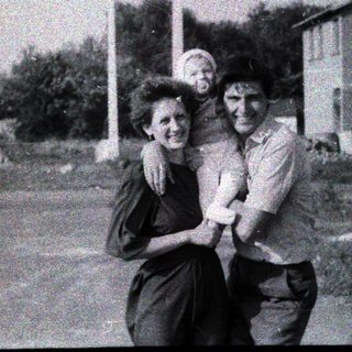 Three people posing happily outdoors in rural setting.