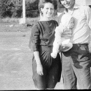 Two adults holding a baby outdoors.