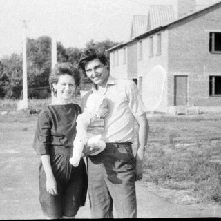 Two adults holding a baby outdoors.