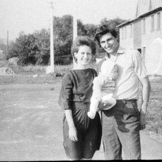 Two adults holding a baby outdoors.