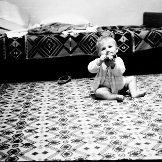 Baby sitting on patterned rug eating.