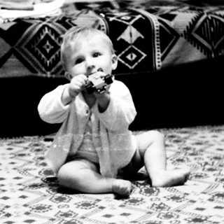 Baby sitting on patterned rug eating.