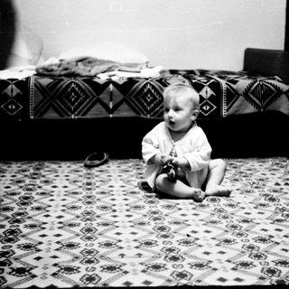 Baby sitting on patterned floor playing with toy.
