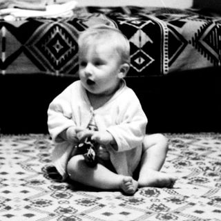 Baby sitting on patterned floor playing with toy.