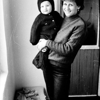 A woman holding a young child indoors near a window.