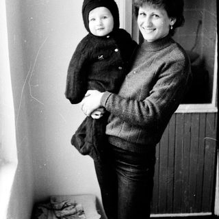 A woman holding a young child indoors near a window.