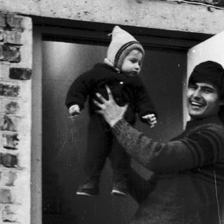 A man joyfully holding a laughing baby at a doorway.