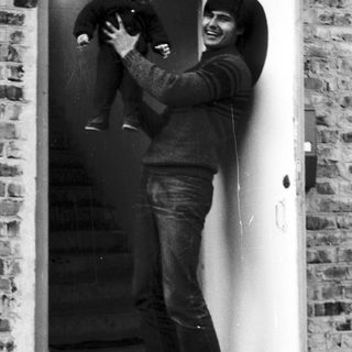 A man joyfully holding a laughing baby at a doorway.