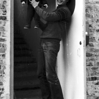 A man joyfully holding a laughing baby at a doorway.