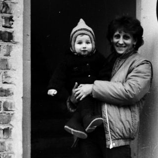 Woman holding child at brick and white door.