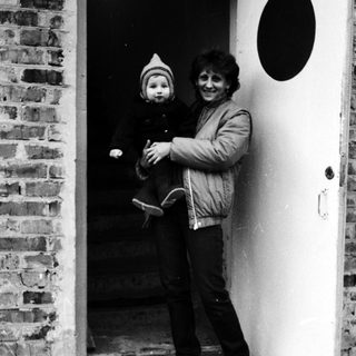 Woman holding child at brick and white door.