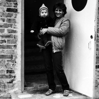 Woman holding child at brick and white door.