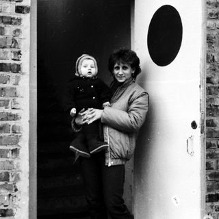 A woman holding a young child near a doorway.