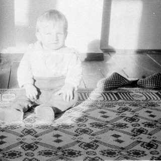 Baby sitting on patterned rug indoors.