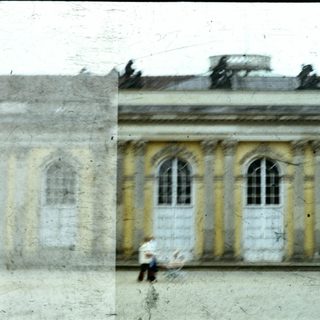 Neoclassical building facade with arched windows, blurred figure walking.