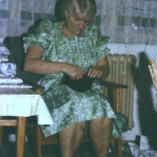 A woman knitting while a child prays or claps.