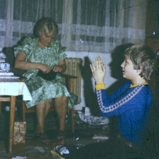 A woman knitting while a child prays or claps.