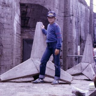 Person holding large concrete slab near old concrete structure.