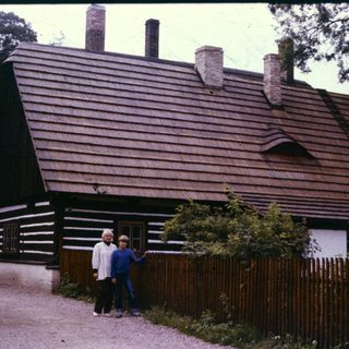 Traditional wooden house with two people posing outside.