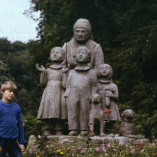 Two people standing beside a family statue in a garden.