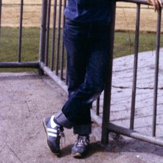 Boy in cap and blue tracksuit posing with skateboard on elevated platform.