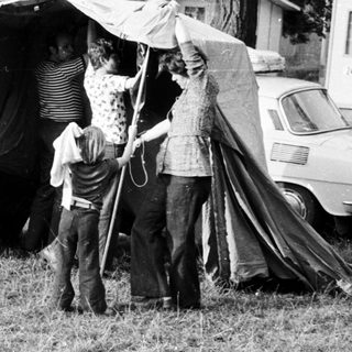 Family pitching tent in grassy campsite area.