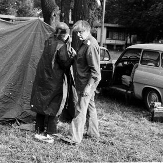 People setting up a tent outdoors near parked cars.