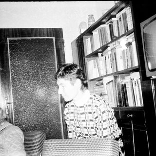 Two people in a dimly lit room with bookshelves.