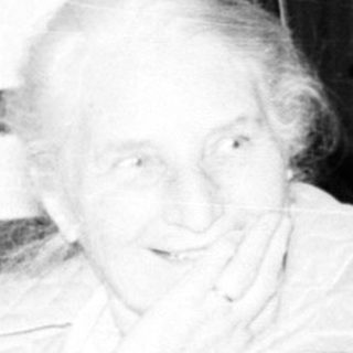 Old woman sitting indoors with family during television broadcast.