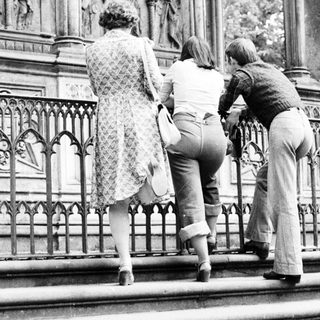 Three people observing ornate stone carvings on a balcony.