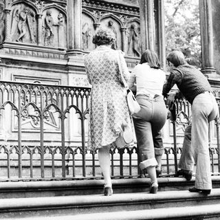 Three people observing ornate stone carvings on a balcony.