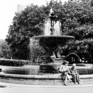 Elegant fountain with water sculptures, two people sitting nearby.