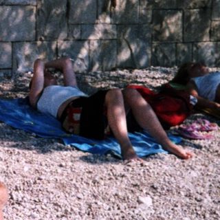 People relaxing on towels and mats by a beach.