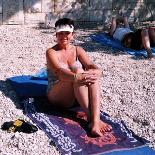 People relaxing on towels and mats by a beach.